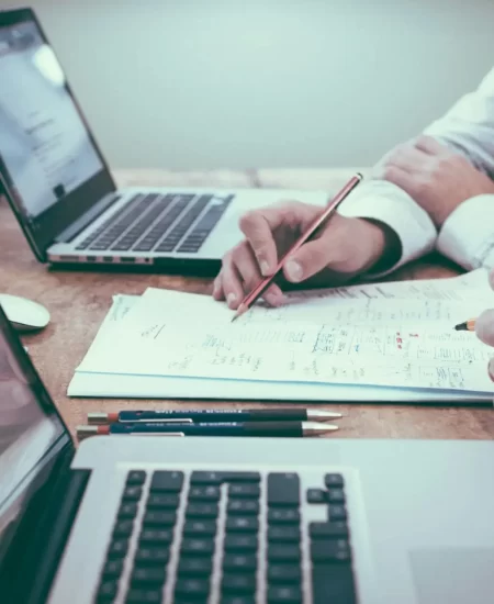 person holding pencil near laptop computer